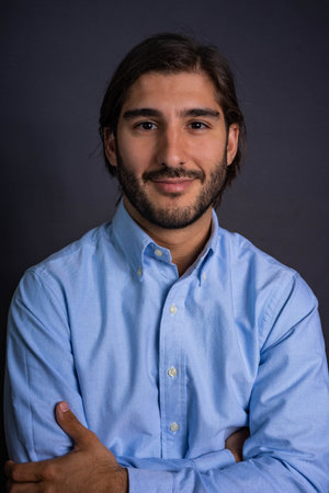 Studio Portrait of Hispanic Man with Beard and Long Hair in Blue Shirt Looking at Camera with...