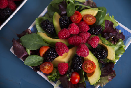 Salad with red berries, cherry tomatoes and avocado, on a blue table.の写真素材