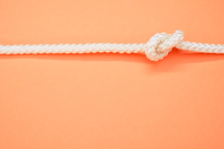 a top view of a white rope with a knot horizontally isolated on the pastel orange backgroundの写真素材