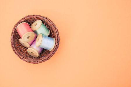 A basket of colorful sewing threads isolated on a pastel orange background with free space for text