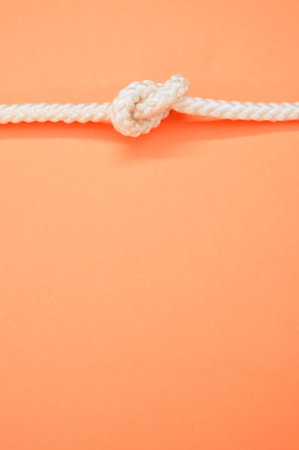 a vertical shot of a white rope with a knot horizontally isolated on the pastel orange backgroundの写真素材