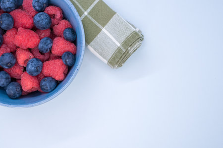 A bowl of fresh berries and a napkin isolated on a blue background with space for textの写真素材