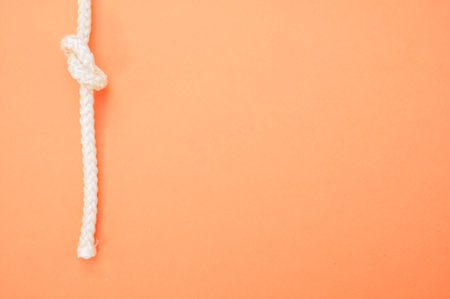 a top view of a white rope with a knot vertically isolated on the pastel orange backgroundの写真素材