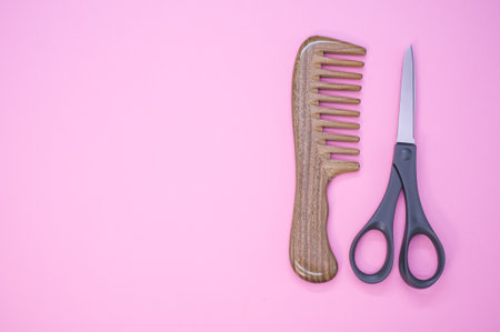 A top view of a hairbrush and scissors on a pink backgroundの写真素材