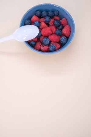 A vertical shot of a bowl of fresh berries with a plastic spoon isolated on a light backgroundの写真素材