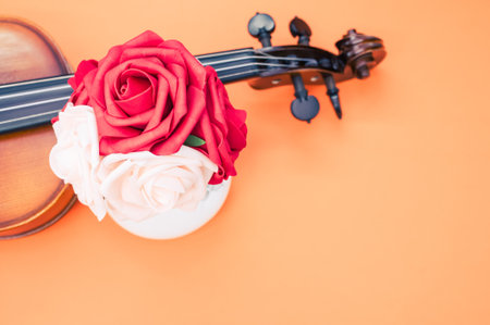 A vertical shot of roses and a violin on orange background with a copy space