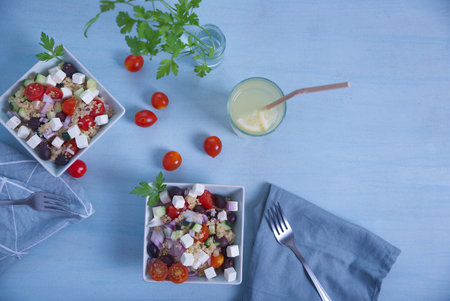 Greek salad in square plates, top view with cherry tomatoes, lemonade, on a light blue background.の写真素材