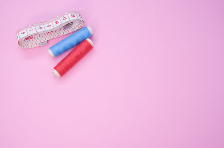 A top view of the colorful sewing threads with a measuring tape on the pink surface
