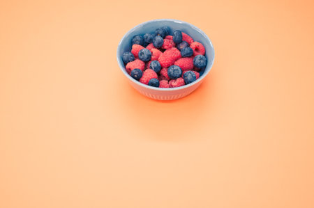 A bowl of fresh blueberries and raspberries isolated on an orange background with space for textの写真素材