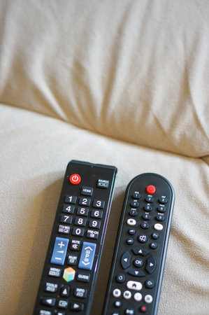 Two black plastic tv remotes on sofa