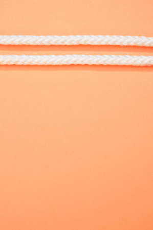 A vertical shot of a rope part isolated on a peach color background