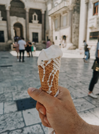 Personal perspective image of man holding ice cream cone with melting and dripping white ice cream.の写真素材