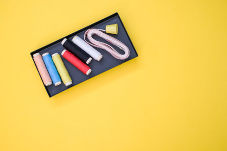 A pack of colorful sewing threads and a measuring tape on yellow background with a copy spaceの写真素材