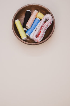 A top view of the colorful sewing threads with a thimble and a measuring tape in the wooden bowlの写真素材