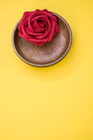 A vertical shot of a red rose flower in a wooden bowl on a yellow surface - beauty and aromatherapyの写真素材