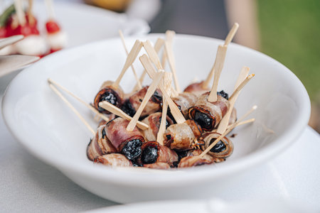 White plate with roasted dried plums wrapped in bacon slices. Sweet salty snack.の写真素材