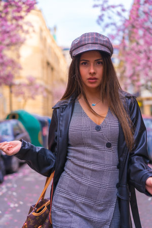Abrunette Caucasian girl in a leather jacket and a beret in the city with the flowered trees in...