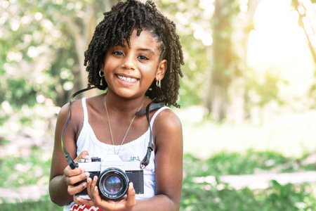 portrait of a young african american toddler girl holding an old camera and looking at camera....