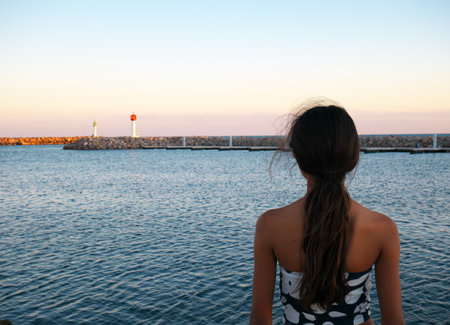 Beautiful photo of a young girl with her back to the sea during the sunsetの写真素材