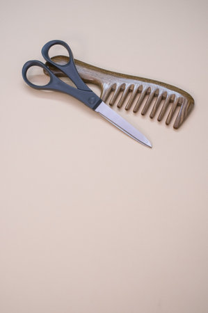 A closeup shot of scissors and hair comb on a beige surfaceの写真素材