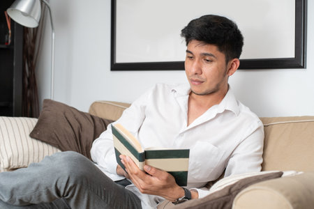 Latin man reading book on sofaの写真素材