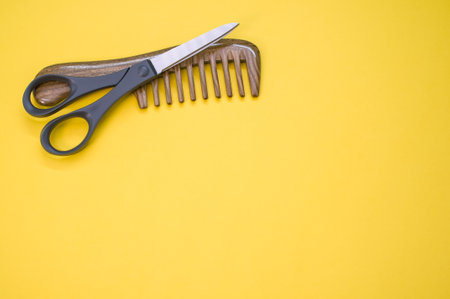 A closeup shot of scissors and hair comb on a yellow surface - copy space