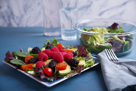 Salad with red berries, cherry tomatoes and avocado, on a blue table.の写真素材