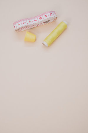 A closeup of a yellow sewing thread with a thimble and a measuring tape on the brown surfaceの写真素材