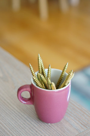 A vertical shot of concrete screws in a colorful cup on a wooden table