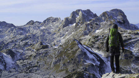 A mountaineer reaches the top of a snowy mountain on a sunny winter day