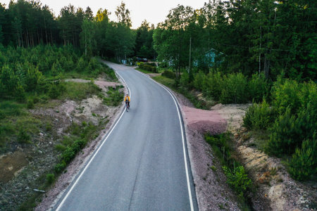 Aerial view following a woman cycling, on a countryside road, sunny, summer evening, in Scandinaviaの写真素材