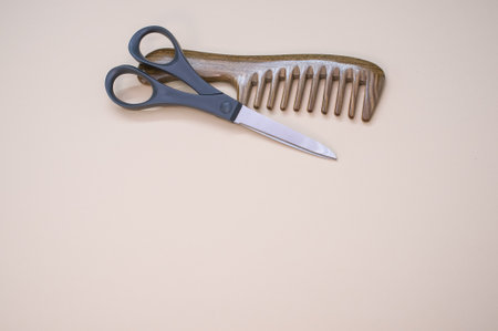 A closeup shot of scissors and hair comb on a beige surface - copy space