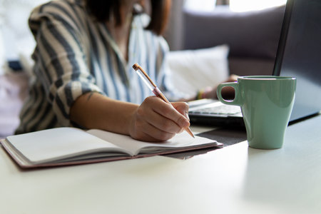 Caucasian white young woman working from home writing in a notebookの写真素材