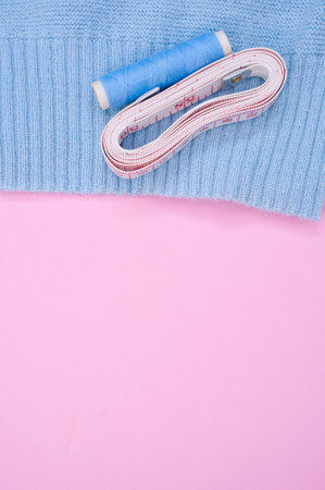 A top view of a blue sewing thread with a measuring tape on the fabric on the pink surface