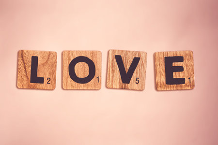 The word "love" written with wooden scrabble tiles on the pink surfaceのeditorial素材