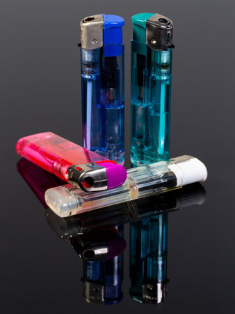 Four gas lighters in different colours on a black reflecting backgroundの写真素材