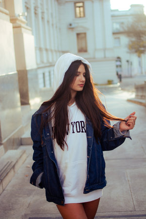 A beautiful Caucasian woman wearing shorts, a jean jacket, and a hoodie walking in the streetの写真素材