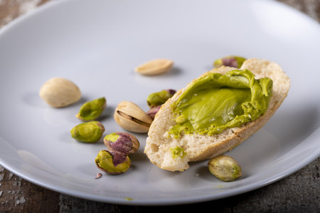 A closeup shot of pistachios and a slice of bread with pistachio spread on a plateの写真素材