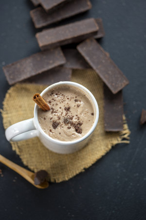 A vertical shot of delicious coffee in a mug with cinnamon and dark chocolate bars