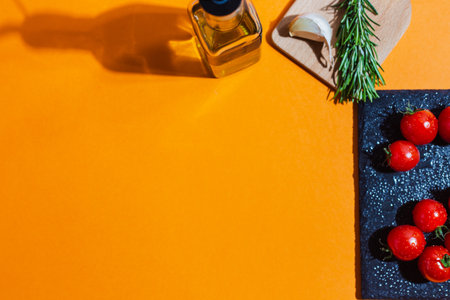 A top view of cherry tomatoes, rosemary, garlic, and olive oil on an orange backgroundの写真素材