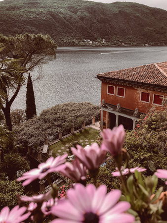 A vertical shot of bright pink flowers in bushes near a villa by a river on a sunny dayの写真素材