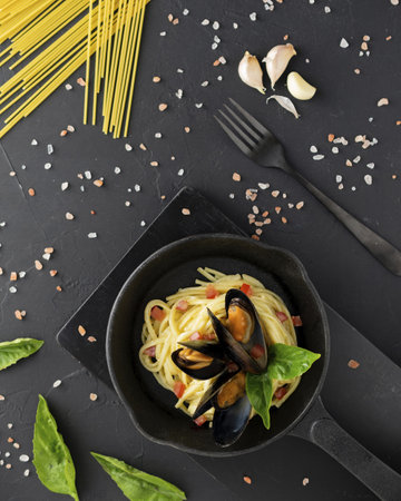 A vertical top view of delicious pasta with mussels, sauce and spices isolated on a black background