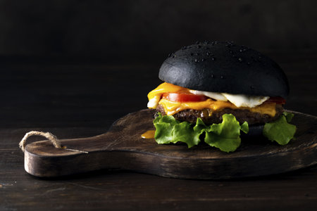 A closeup shot of a tasty beef cheeseburger with melted cheese isolated on black backgroundの写真素材