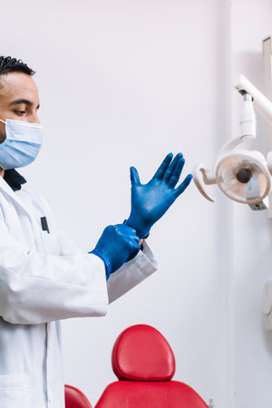 An adult dentist with a medical face mask putting on blue latex glovesの写真素材