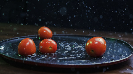 A closeup shot of cherry tomatoes with water droplets on the black plateの写真素材