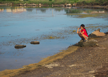 photo of a little girl sitting by the pond during the sunsetの写真素材