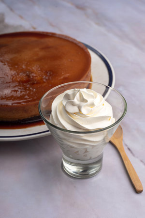 A vertical closeup shot of whipping cream in a glass next to a cake