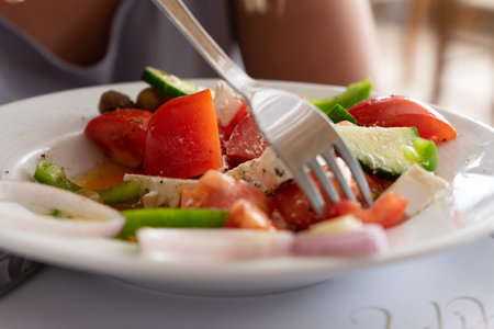 A closeup of a person eating a delicious salad with tomato, cucumber, cheese, and onionsの写真素材