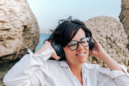 Portrait of young woman with eyeglasses enjoying while listening to music on beach.