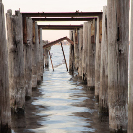 A wooden pier with weathered columns in the sea on background of the sky